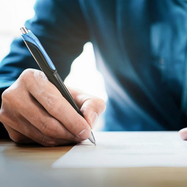 Person holding a pen, writing on a piece of paper.