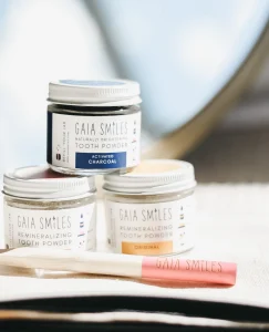 Three jars of tooth powder sit with a gaia smiles branded tooth brush.