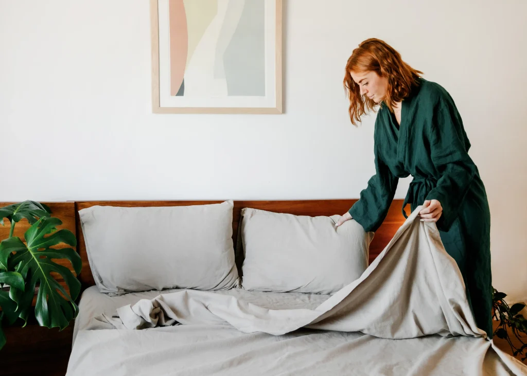 A woman pulls up a grey linen bedsheet.