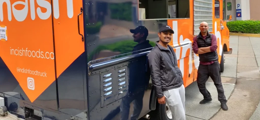 Indish owners lean against their food truck.