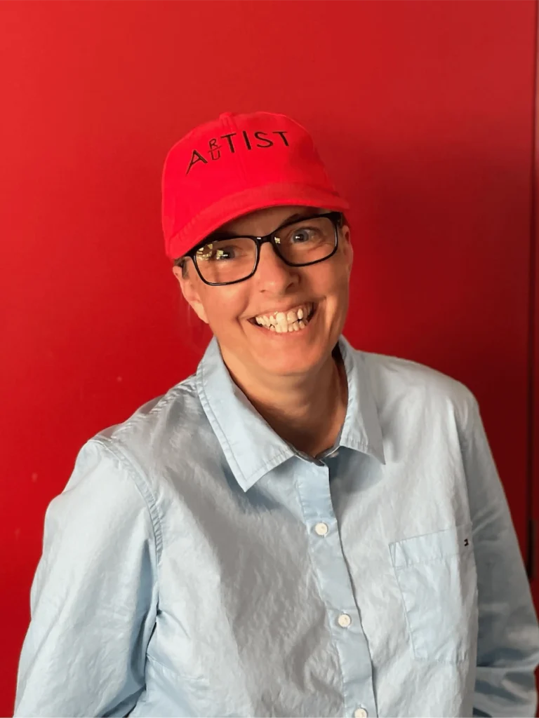 Jenine Lillian smiling and wearing a red hat in front of a red background.