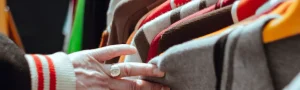 A view of a person's hand looking through a rack of shirts.