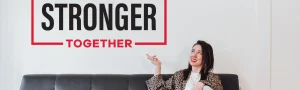 Foxy Box Founder and CEO, Kyla Dufresne, sitting on a black couch in front of a white wall with a sign that says "We're stronger together".